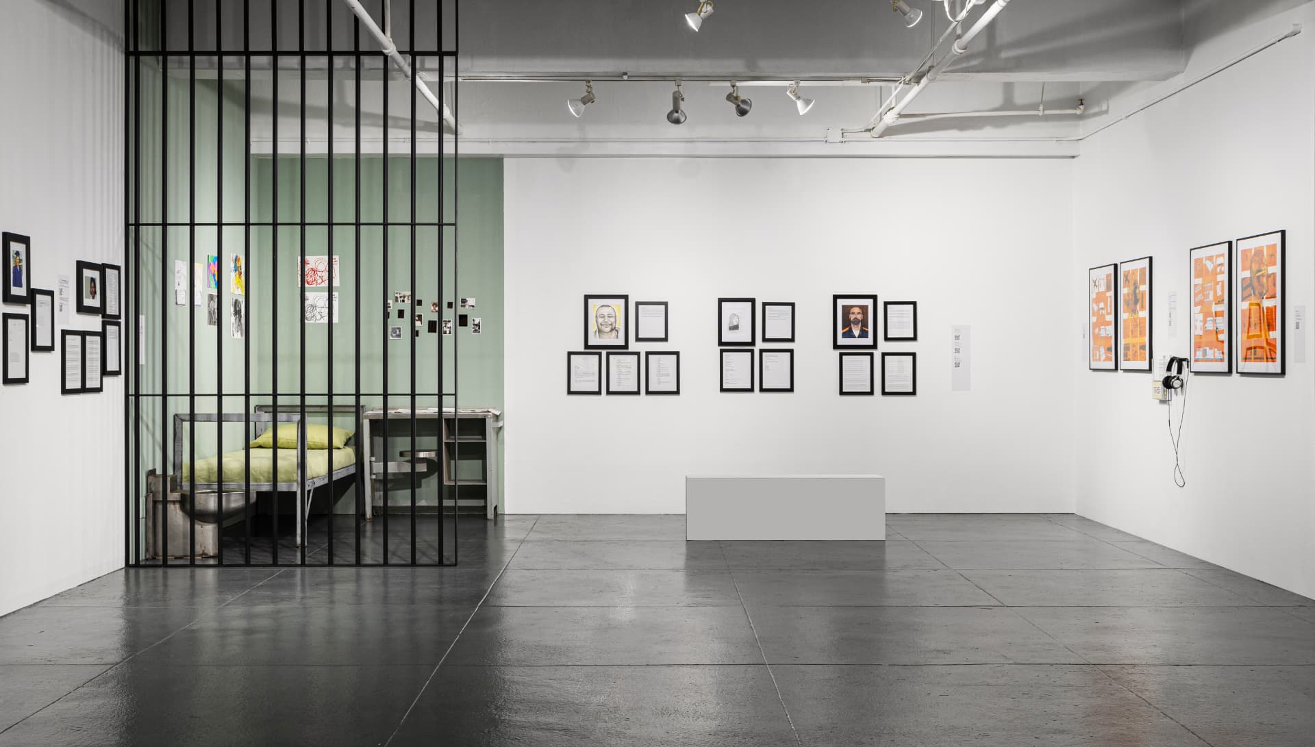 Gallery view of Return to Sender: Prison as Censorship at EFA Project Space, with a recreated prison cell behind bars and framed portraits and writing on the walls.